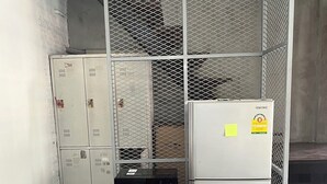 A compact kitchen with a microwave on a wooden stool, a refrigerator, and metal lockers. - Siam Breeze Inn - Self Check-in (Bangkok)