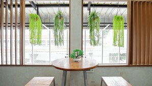 A room with a round wooden table, two metal stools, and hanging green plants. - Siam Breeze Inn - Self Check-in (Bangkok)