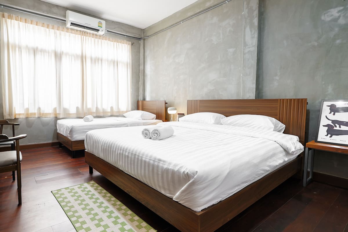 A hotel room with two beds, a wooden headboard, a green and white patterned rug, a wooden chair, and a framed picture on the wall.