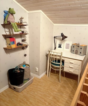 A child's room with a desk, chair, shelves with toys, and books.