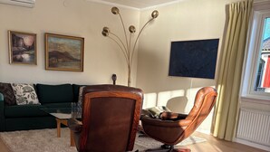 A living room with a green sofa, two leather chairs, a coffee table, and a TV. There are paintings on the wall, a guitar, and a vase with branches. - Lake House Retreat with a Dock & Boat (Västra Götalands län)