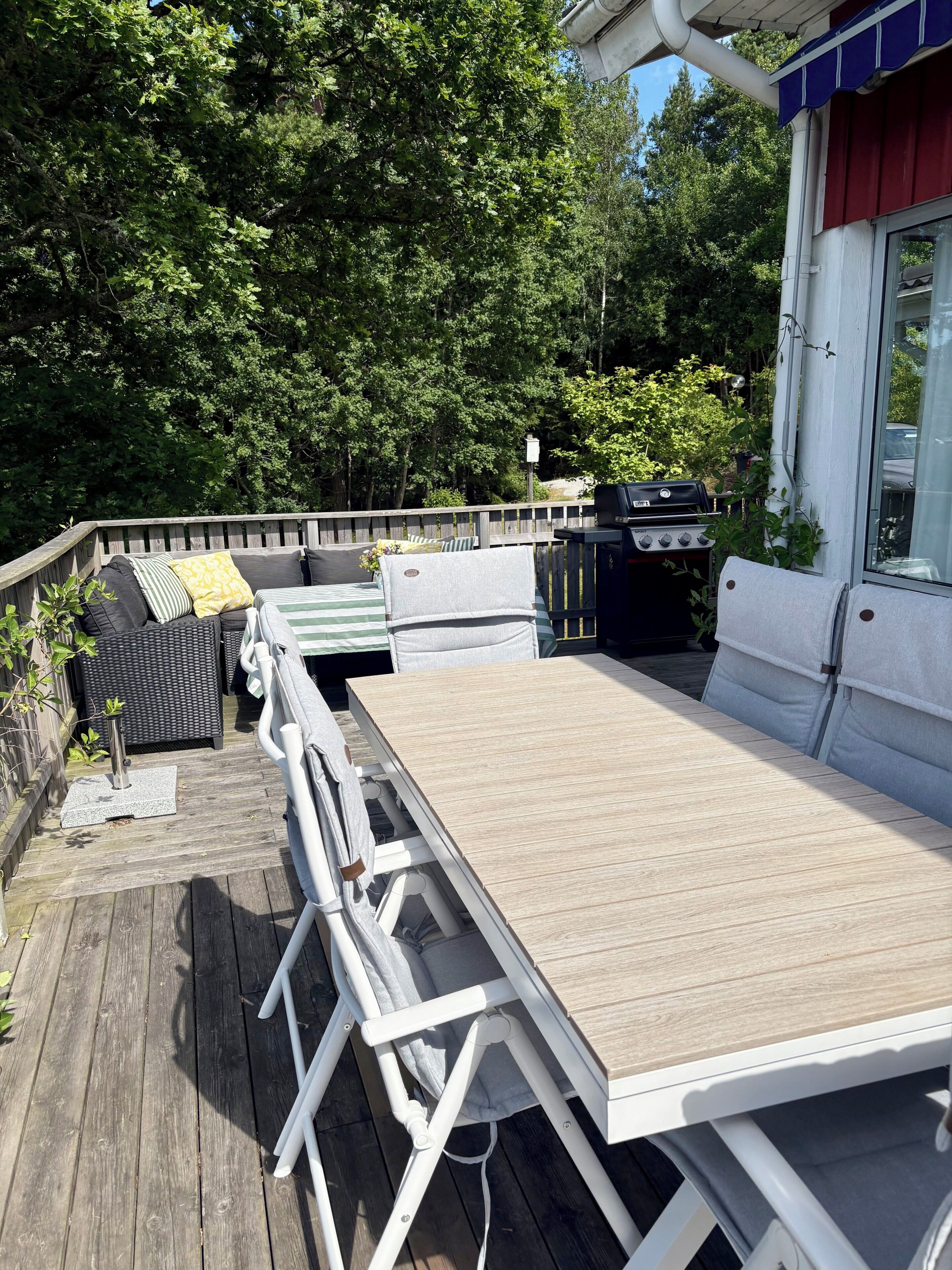 An outdoor deck with a table and chairs, a grill, and a view of the surrounding greenery.
