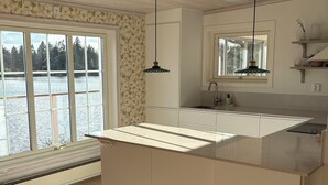 A modern kitchen with a large island, wooden flooring, and a view of a lake. - Lake House Retreat with a Dock & Boat (Västra Götalands län)
