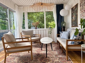 Un salon confortable avec un canapé, des fauteuils, une petite table et une grande fenêtre agrémentée de rideaux.