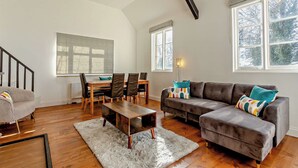 Ein geräumiges Wohnzimmer mit Holzboden, einem grauen Sofa, einem Esstisch mit Stühlen und einer Treppe.