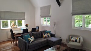 Ein modernes Wohnzimmer mit einem Ecksofa, einem kleinen Tisch und einem Essbereich mit einem Stuhl und einer Blumenvase.