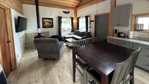 A cozy cabin interior with a wooden ceiling, a sofa, a dining table, and a kitchen area. - Ocean front 2-bedroom cabin in Whale Pass with strong WiFi (Whale Pass)