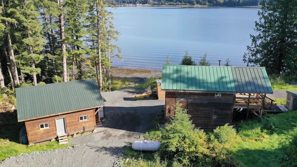 A cabin with a green roof and a wooden structure, surrounded by trees and a lake. - Ocean front 2-bedroom cabin in Whale Pass with strong WiFi (Whale Pass)