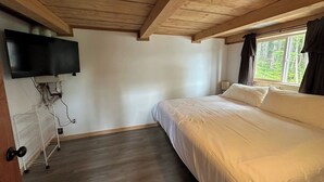 A bedroom with a wooden ceiling, a bed, a TV mounted on the wall, and a window with curtains. - Ocean front 2-bedroom cabin in Whale Pass with strong WiFi (Whale Pass)