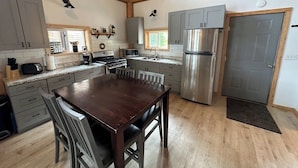 A spacious kitchen with wooden beams, grey cabinets, stainless steel appliances, and a central dining table. - Ocean front 2-bedroom cabin in Whale Pass with strong WiFi (Whale Pass)