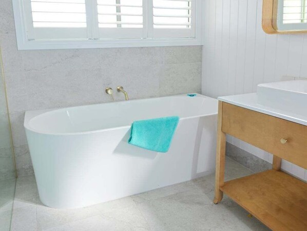 A bathroom with a white bathtub, a wooden vanity, and a window with blinds. - Beilby Inlet Views I Walk to beach and town centre (Bass Coast)