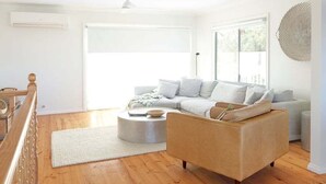 Ein modernes Wohnzimmer mit einem beigefarbenen Sofa, einem weißen Couchen und Holzboden.