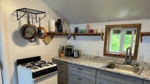 A kitchen with a stove, sink, and wooden shelves.