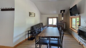 A dining area with a long table and chairs, a fireplace, a television, and a window with curtains.