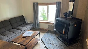 A living room with a sofa, a wooden coffee table, a stone fireplace, and a window with curtains.
