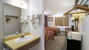 A hotel room with a bathroom featuring a sink and mirror, a bed with a patterned bedspread, and a microwave on a counter.