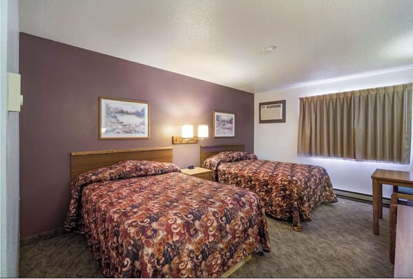 A hotel room with two beds, a small table, and two wall-mounted lamps.