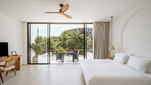 Une chambre d’hôtel moderne dotée d’un grand lit, d’un bureau avec une chaise, d’un balcon avec une table et des chaises, et d’un ventilateur de plafond.