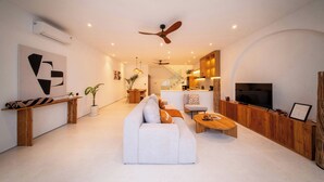 Un salon moderne avec un canapé blanc, une table basse en bois et un téléviseur posé sur un meuble en bois.