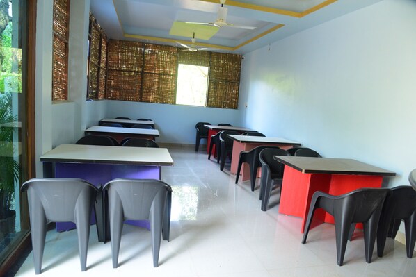 A classroom with desks and chairs arranged in rows, a ceiling fan, and a window with bamboo blinds.