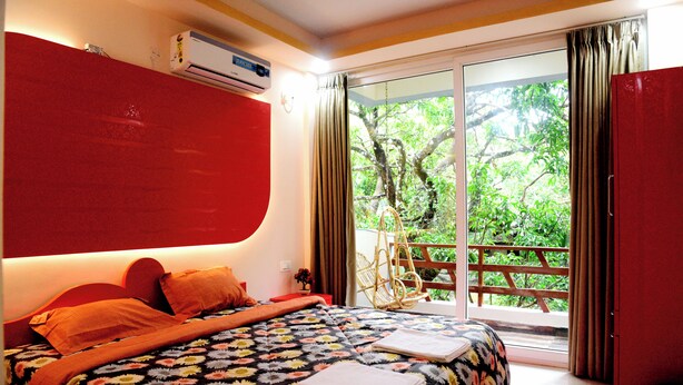Ein Schlafzimmer mit einem großen Bett, einer roten Wand und Blick auf Grün durch eine Schiebetür.