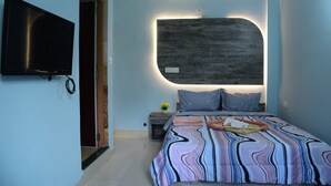 Ein modernes Schlafzimmer mit einem großen Bett, einem flachbildfernseher an der Wand und einem Nachttisch mit einer Lampe.