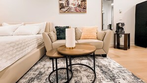 A modern hotel room with a bed, a sofa, a coffee table, and a painting on the wall. - Tastefully furnished new studio in Bear Mountain (Langford)