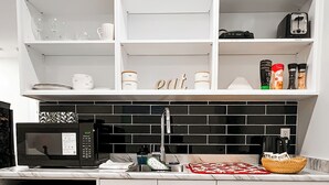 A compact kitchen with white cabinets, a black tiled backsplash, a microwave, a toaster, and a sink. - Tastefully furnished new studio in Bear Mountain (Langford)
