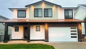A two-story house with a garage, a covered porch, and a well-maintained lawn. - Tastefully furnished new studio in Bear Mountain (Langford)