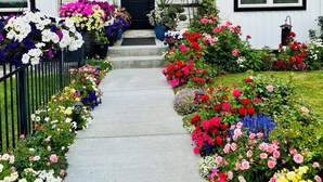 A two-story house with a black front door, a small porch, and a front yard with colorful flowers and a black metal fence.