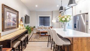 A modern kitchen with a central island, bar stools, and a dining area with a sofa.