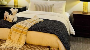 A bedroom with a bed, two bedside tables, a cityscape painting, and a ceiling light.