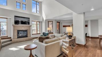 Relax in a spacious living area with a high ceiling and large windows, a comfortable seating area, and a fireplace.