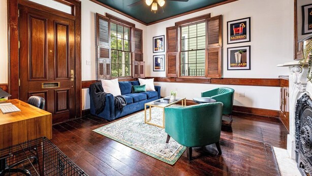 Un salon spacieux doté d’un plancher en bois, d’un canapé bleu, de fauteuils verts et d’un ventilateur de plafond.