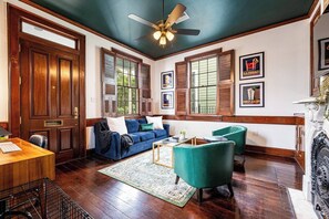 A spacious living room with a wooden floor, a blue sofa, green armchairs, and a ceiling fan. - The Channel Gem: Remote Work & Relaxation Haven (New Orleans)
