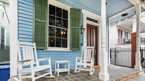 Une véranda avec deux fauteuils à bascule et une petite table, une porte avec une fenêtre et un mur en briques.