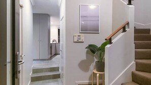 A staircase with a wooden handrail, a potted plant on a small stool, and a wall-mounted light fixture.