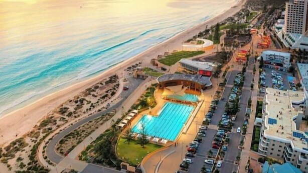 An aerial view of a coastal resort with a swimming pool, parking area, and beachfront.