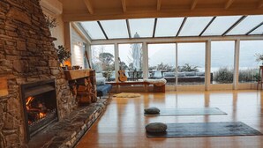 A spacious living room with a stone fireplace, yoga mats, and a large window overlooking a snowy landscape.