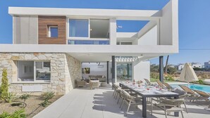 A modern two-story house with a stone facade, a dining area with outdoor seating, and a pool.