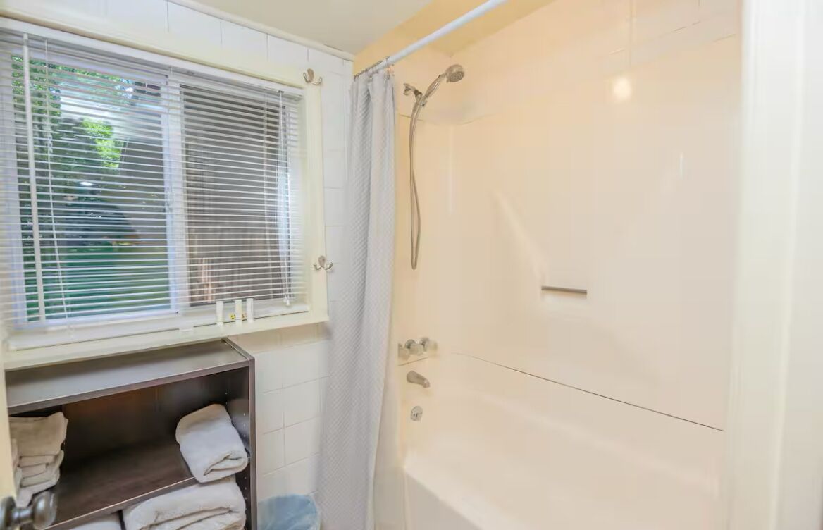 A bathroom with a bathtub, a shower, and a window with blinds.