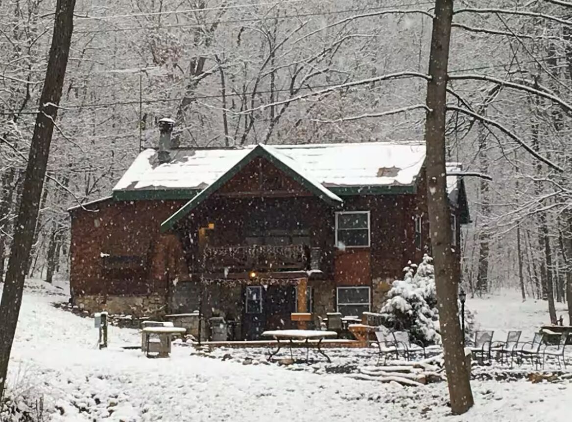 Un chalet rustique, dont le toit est recouvert de neige, entouré d’arbres.