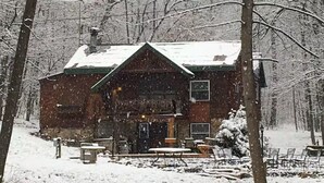 Una cabaña rústica con techo cubierto de nieve, rodeada de árboles.