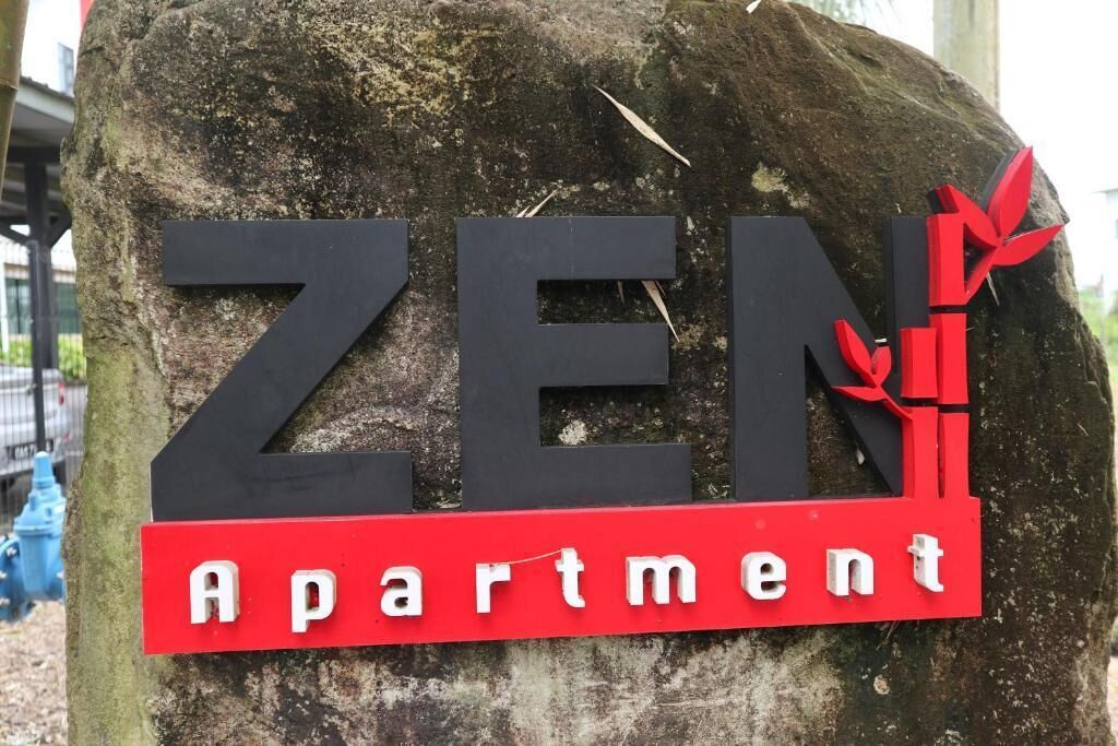 Un letrero que dice 'ZEN Apartment', con letras negras grandes y un cartel rojo en la parte inferior.