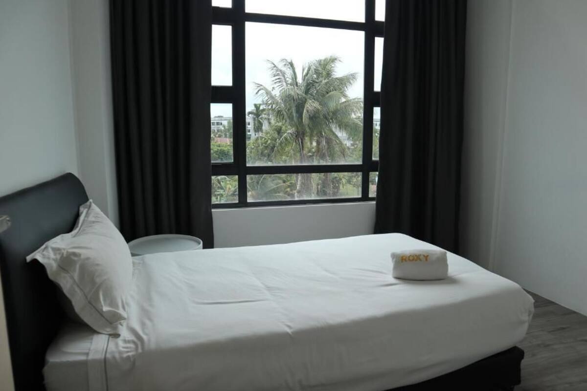 A hotel room with a bed, a window with curtains, and a view of palm trees outside.