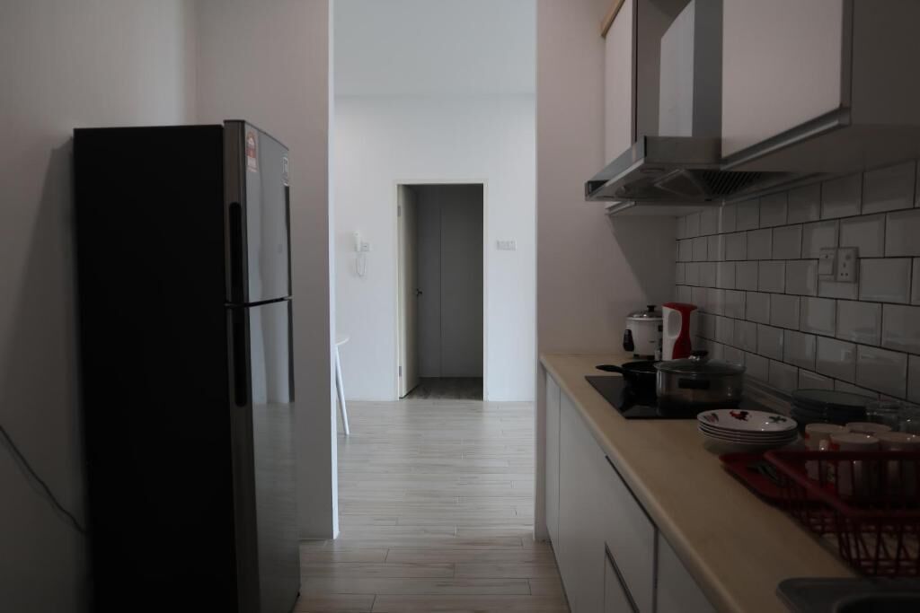 A narrow kitchen with a black refrigerator, white cabinets, and a tiled backsplash.