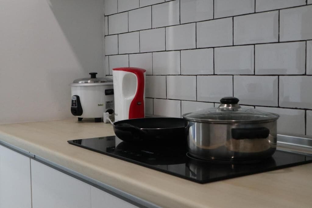 A kitchen with a black induction cooktop, a stainless steel pot, a red and white electric kettle, and a white appliance with a black control panel.