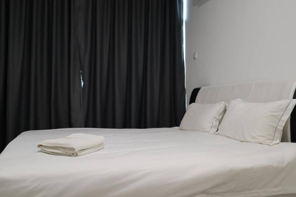 A neatly made bed with white linens and pillows, a dark curtain backdrop, and a white wall.