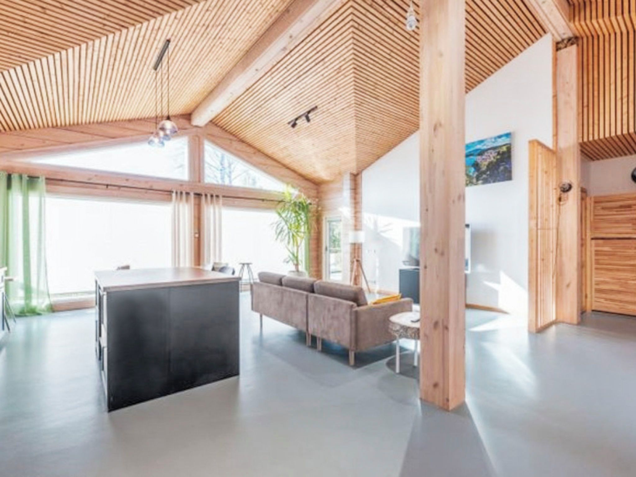 Een modern interieur met een houten plafond, een bank, een eethoek en een groot raam.