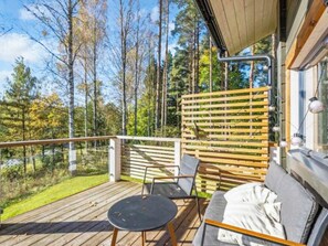 Une terrasse en bois avec un canapé et une table, donnant sur une zone boisée.